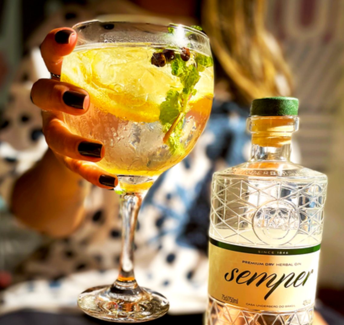Post da Semper Gin: taça de gin tônica com limão e hortelã ao lado da garrafa